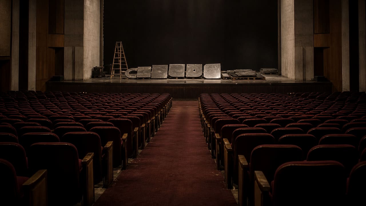 Rows of empty red theater seats face a dark stage where blank metal facade pieces and a work ladder have been stored.