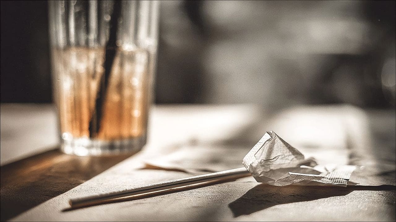 A crisp plastic drinking straw standing upright in a glass of iced tea beside a soggy, collapsed paper straw.